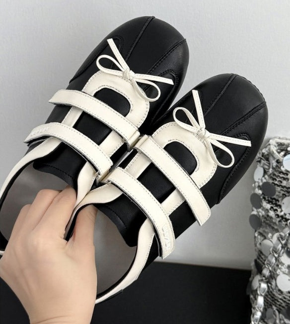 A pair of black and white platform caged sandals with white ribbon bows, held by a hand against a neutral gray background.
