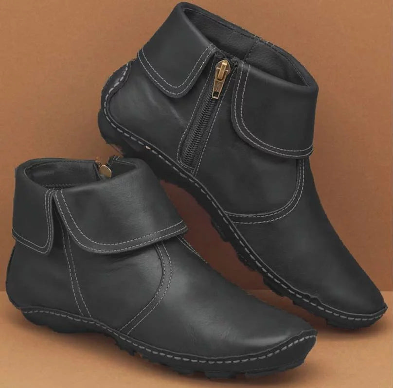 A pair of black leather ankle boots with side zippers, shown on a solid brown background.