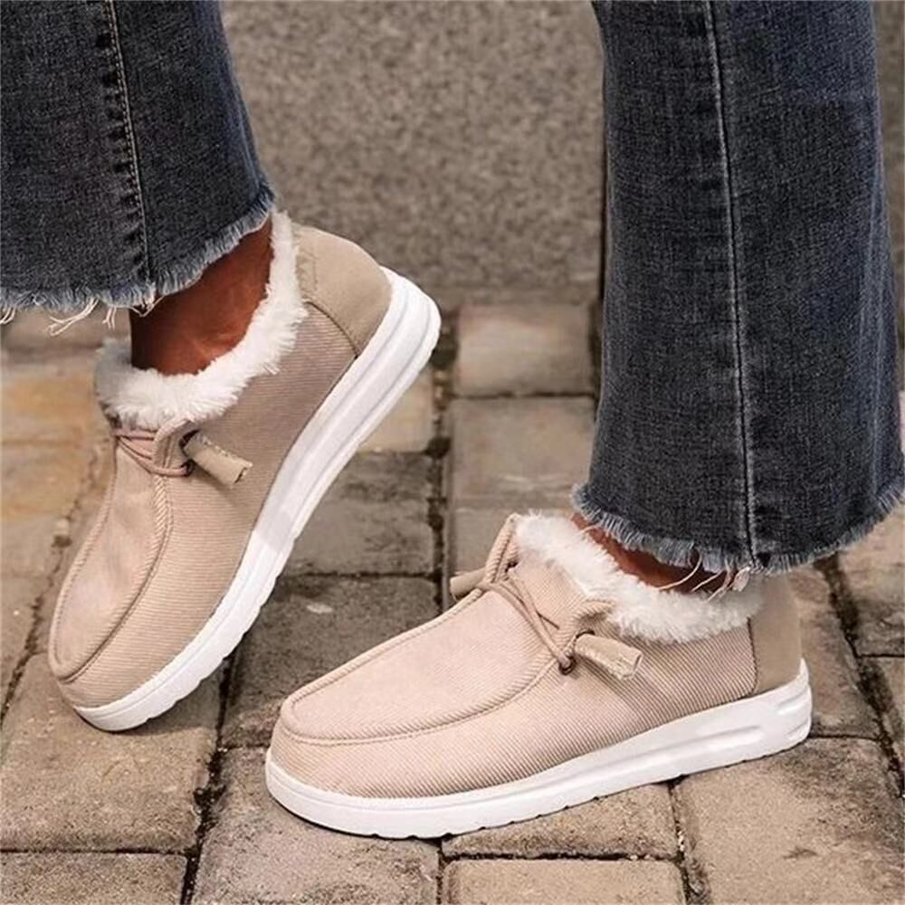 Beige winter boots with white soles worn by a person on a stone pavement.
