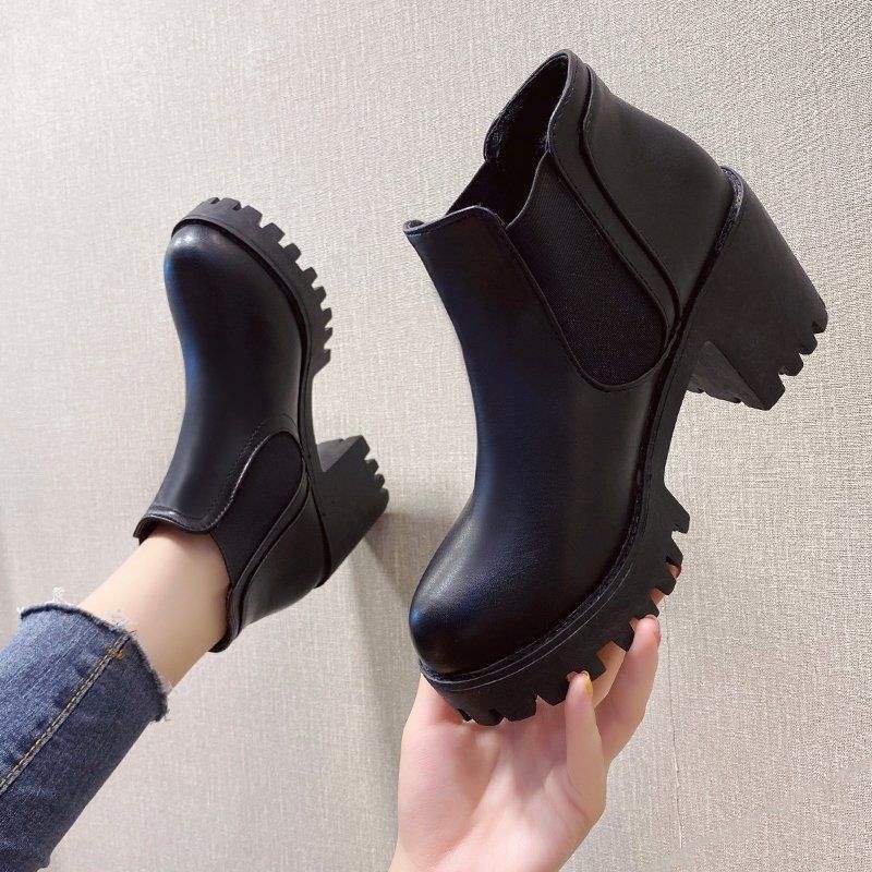 Black ankle boots being held against a neutral background