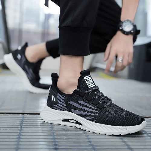 Black athletic shoes with white soles worn by a person on a tiled floor.