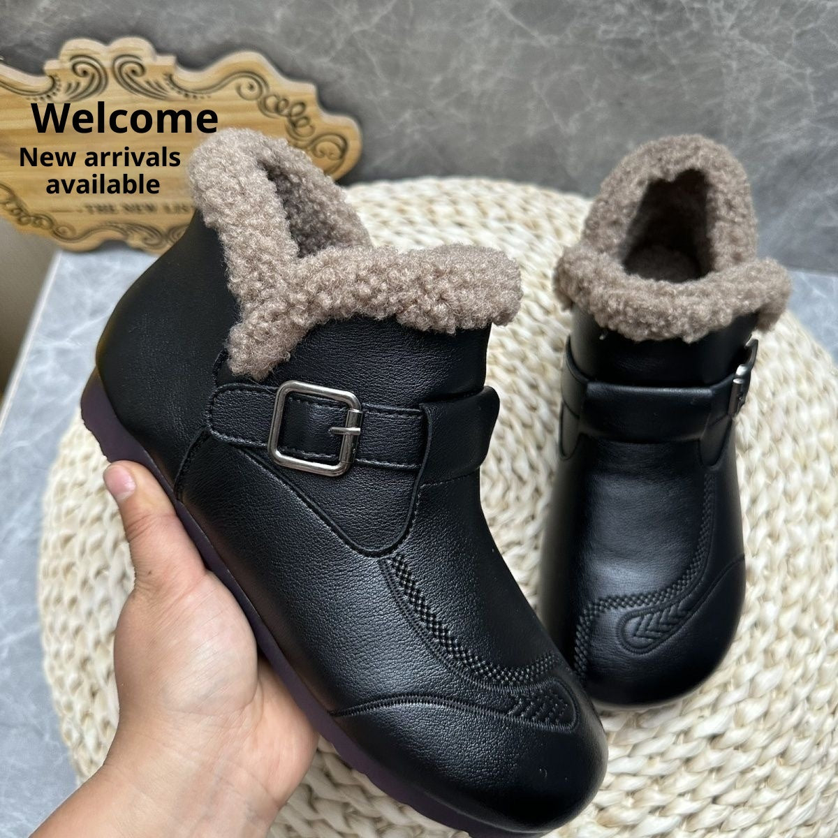 Black children's boots with fur lining held by a hand on a textured surface.
