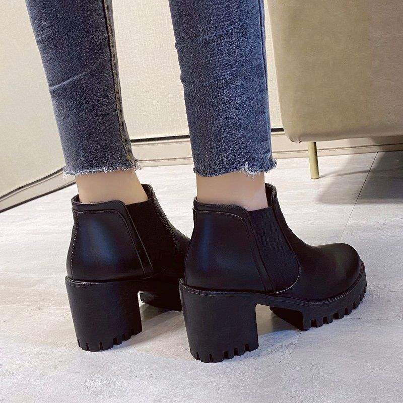 Black chunky-heeled ankle boots worn with blue jeans on a light floor.