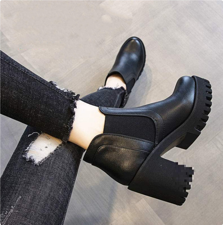 Black chunky platform boots worn with ripped jeans on a light wooden floor.