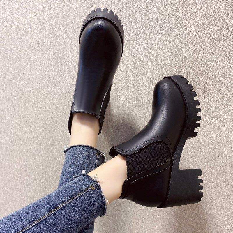 Black platform shoes worn with blue jeans on a neutral background