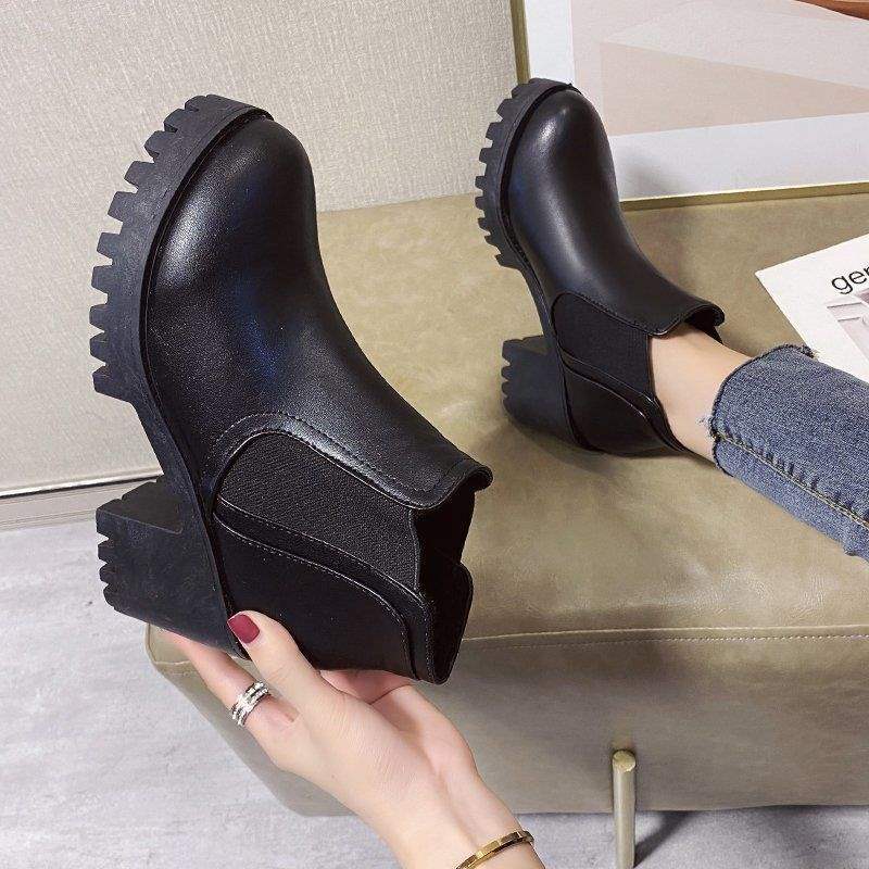 Black rubber boots with unique sole design held by a hand on a neutral background