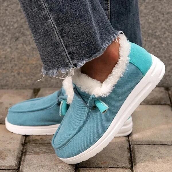 Blue winter boots with white fur lining worn by a person on a stone pavement.