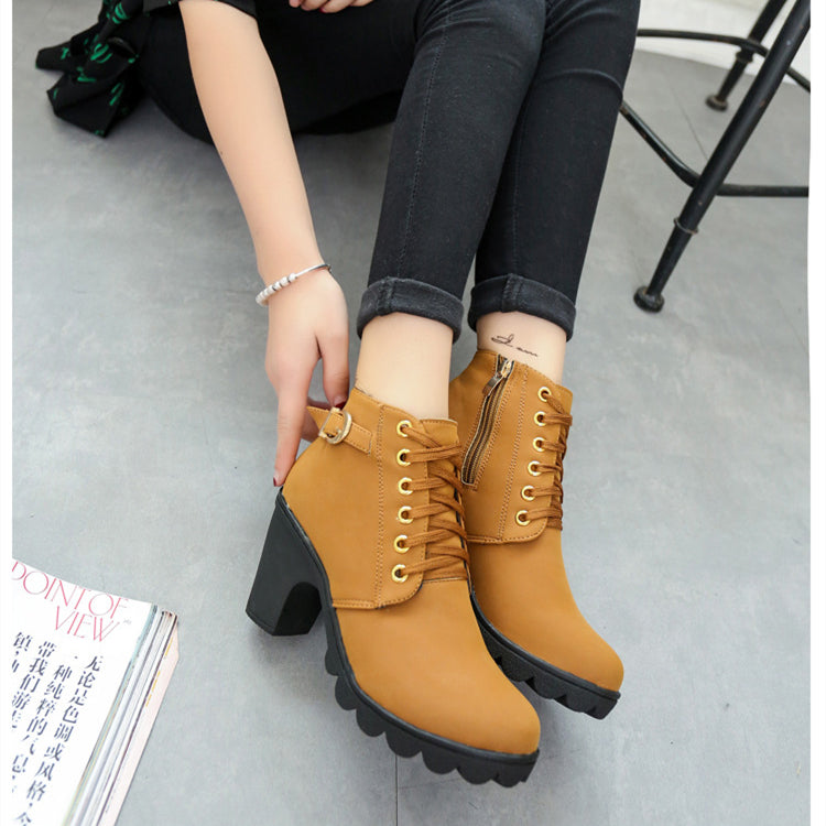 Brown ankle boots with black soles worn by a person on a gray floor.