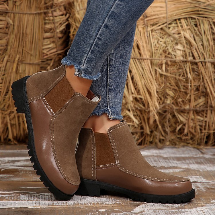 Brown leather boots with black soles worn by a person against a rustic background.