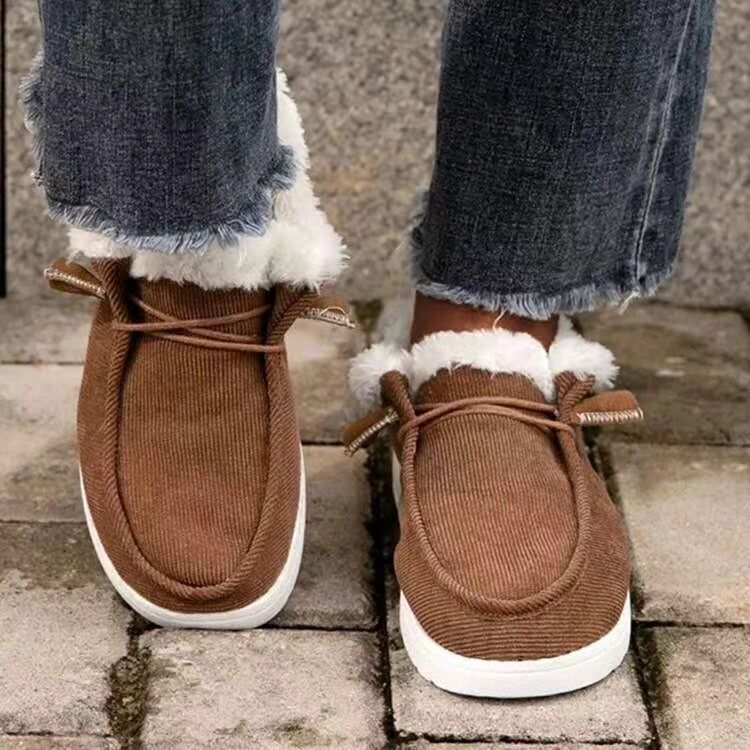 Brown moccasin shoes with white soles worn with blue jeans on a stone surface.