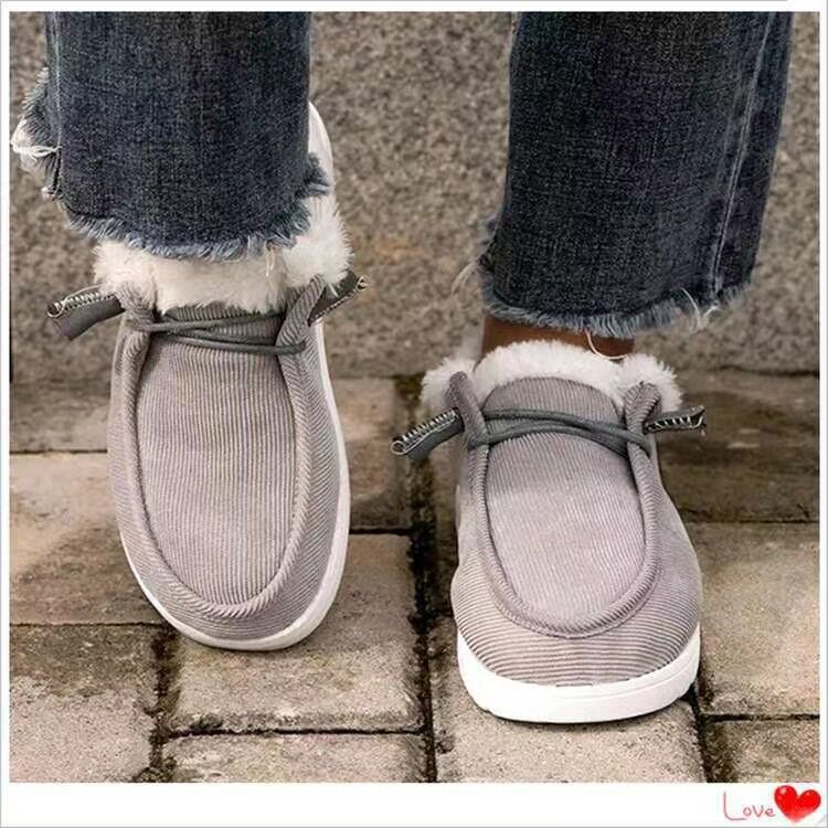 Gray slippers with white fur trim worn with blue jeans on a stone floor.