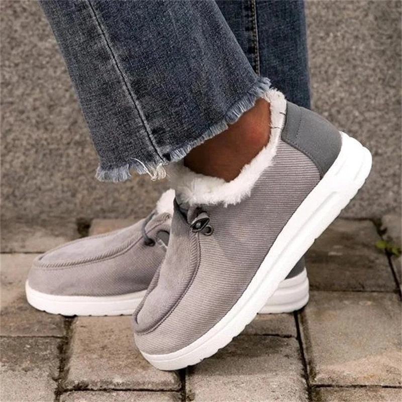 Gray winter boots with white fur lining worn with blue jeans on a stone surface.
