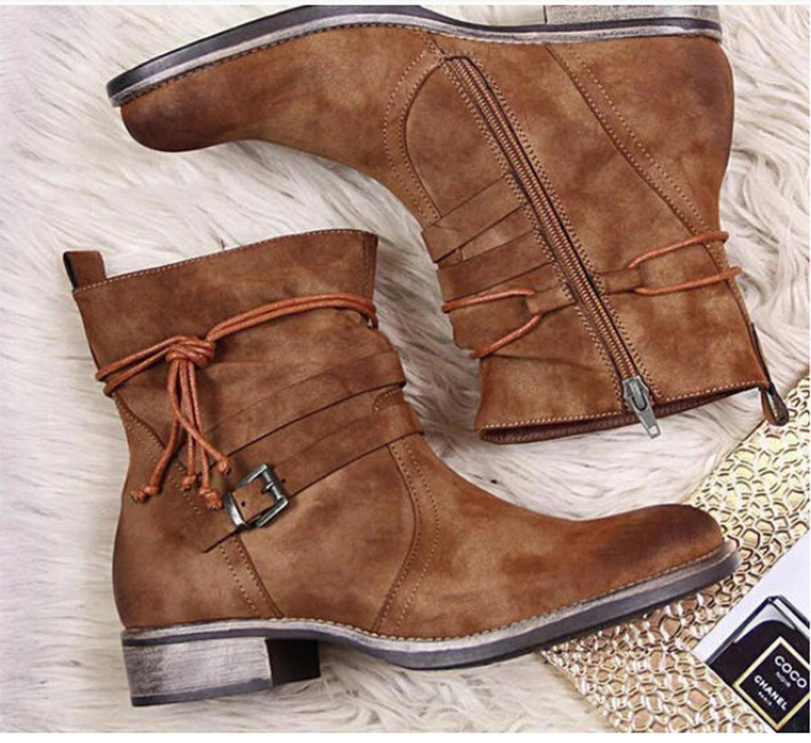 Pair of brown leather boots with a buckle on a textured surface
