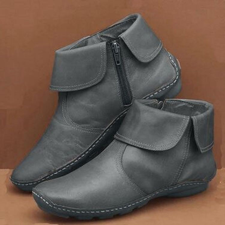 Pair of gray ankle boots with a zipper on a brown background