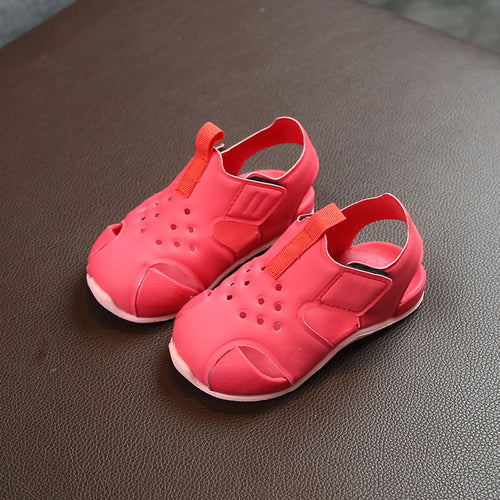 Pair of red children's sandals with orange straps on a brown surface