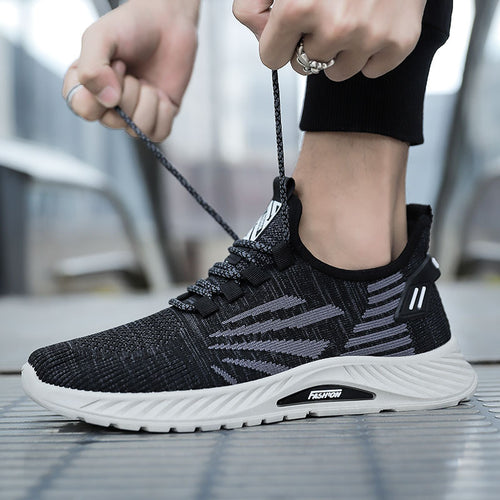 Person tying the laces of a black and gray athletic shoe with a blurred background