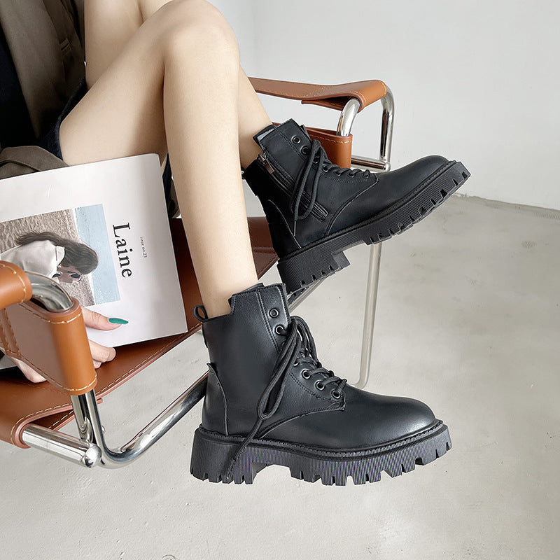 Person wearing black boots sitting on a chair with a magazine.