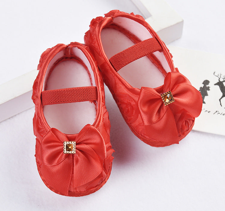Red baby shoes with bow details on a white background