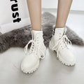 White lace-up boots worn by a person on a light gray surface with a fluffy rug in the background.