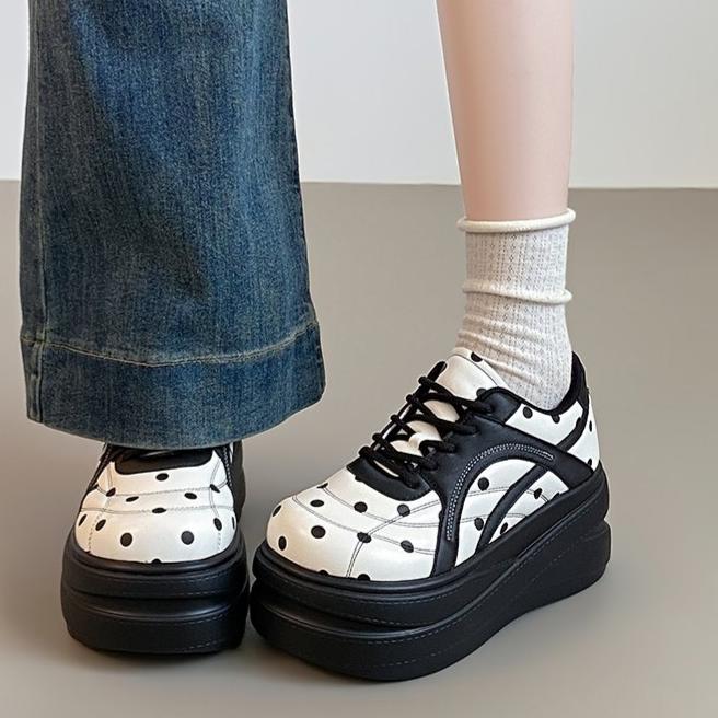 White platform sneakers with black polka dots, worn with black-and-white socks and blue jeans.